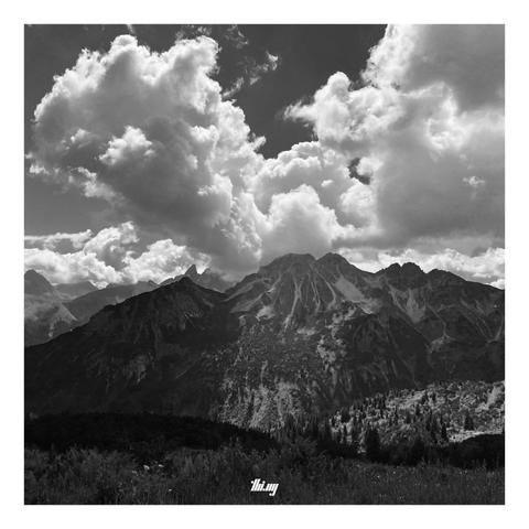 Black and white photo of a layered mountain range partially illuminated by a gap in the (large cumulus) clouds.