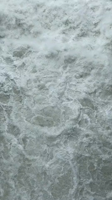 A short video showing a large 30 meter wide waterfall (originally natural, but meanwhile re-engineered for hydro energy purposes) filmed from the footbridge above the pool and panning slowly upward. Intense water flow, spray & volume. The water color is milky gray/green.