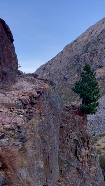 360 video panning of a narrow, rocky footpath (partially secured with steel ropes) around 100 meters above a narrow canyon, higher up opening into a vast high alpine valley...