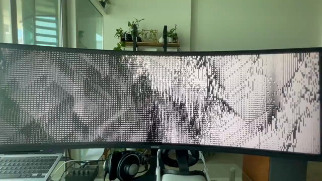 Short video of a B&W variation of ASCII-SCAPE running on a super-widescreen curved monitor. After a few seconds, the camera is moving much closer to the screen to only show a close-up of a handful of text characters making up the complex, vertically scrolling and evolving larger pattern.