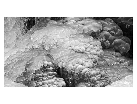 B&W photo of smooth bubble-like ice structures and forms at the bottom of a large waterfall, with a semi-organic feel to it, like an alien organism growing...