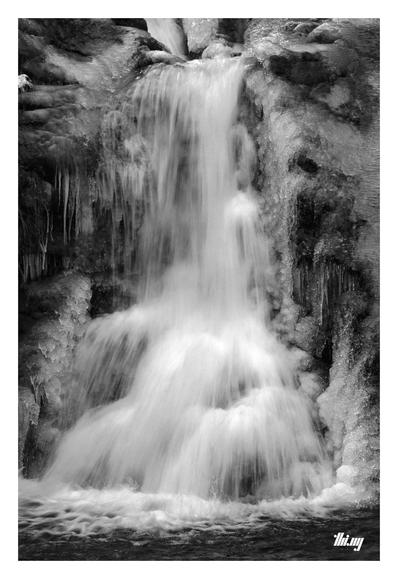 Long-exposure B&W photo of a waterfall crashing down some rocks, completely encrusted in layers of ice.