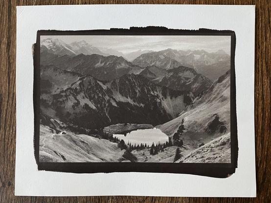Phone picture of a 8x10" sheet of paper with a smaller kallitype print of a multi-layered high alpine mountain landscape with a small mountain lake in the foreground and snow capped mountains in the back.
