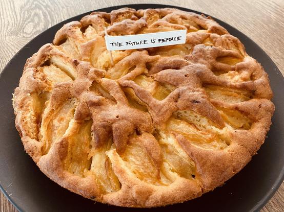 Photo of a freshly baked apple cake with a small flag saying "the future is female"...