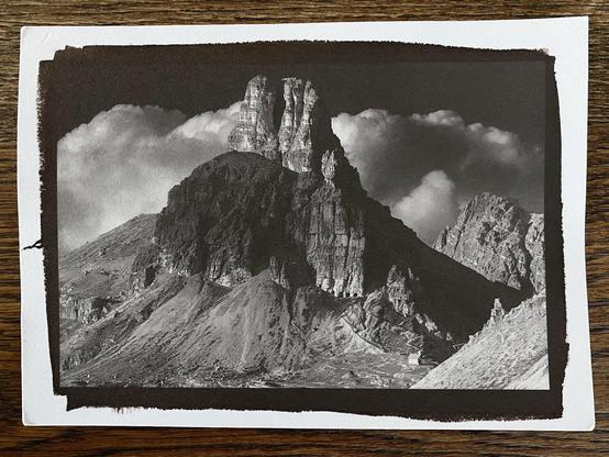 Phone photo of a handmade 6x4" high contrast kallitype print of a rock tower in the Dolomites with epic cumulus clouds in the background.
