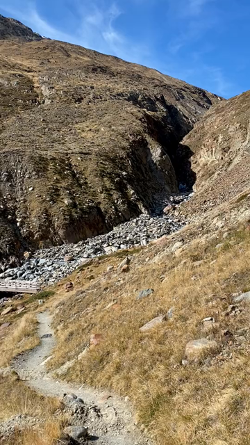 300 degree video panorama/pan of a high alpine landscape showing the confluence of two former glaciers, now reduced to rocky river beds cutting through canyons in a vast tree-less landscape shaped by glacial activity. Snow capped mountains in the distance. Sunny day with semi-overcast blue sky.