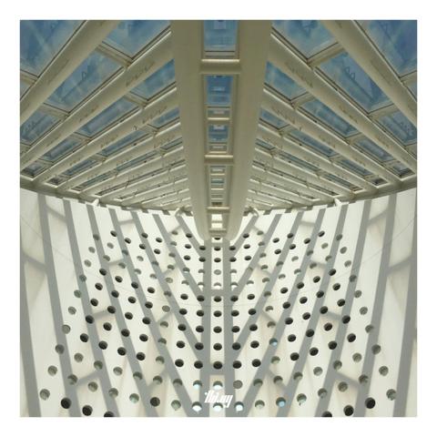 Abstract photo of a light well with patterned, fishbone-like window on top and circular holes in the wall opposite the viewer.