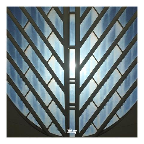 Abstract photo of a cylindrical light well with patterned, fishbone-like window at the top. Close up view from below.