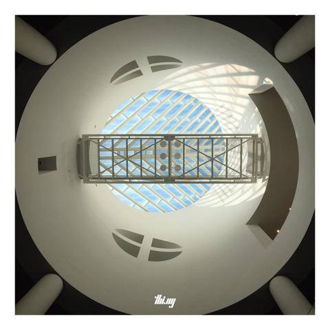 Abstract photo of a cylindrical light well with patterned, fishbone-like window at the top and a gangway leading across. View from below.
