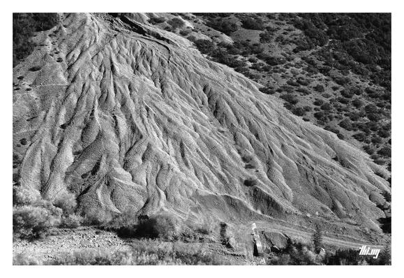 B&W photo of a dune-like growing scree field caused by regular rock falls, semi-guided/funneled by man-made infrastructure.