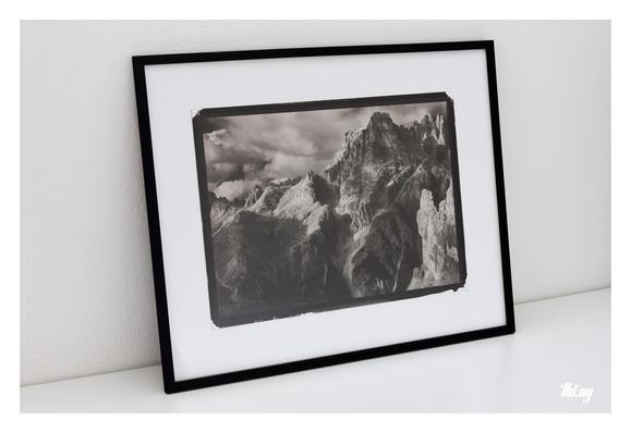 Photo of a 15x11" handmade kallitype print of a moody mountain landscape, framed in a 50x40cm thin black frame, leaning against a white wall.