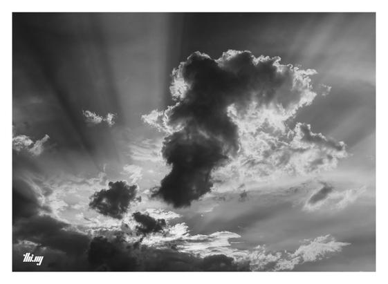 B&W photo of storm clouds with spectacular light shafts emanating from behind the lower cloud layers and across the sky