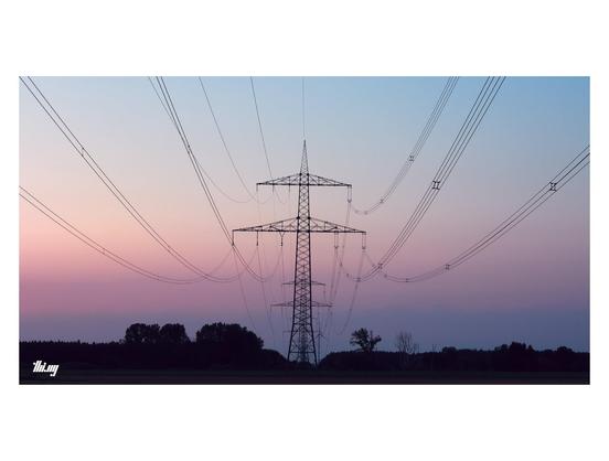 Wide-format photo of the silhouettes of some electricity masts and trees against a clear summer evening sky with post-sunset gradient of soft purple, pink, orange and blue.