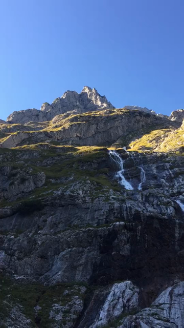 Short video panorama following the flow of a waterfall emerging from the rocks above and flowing into a mountain creek