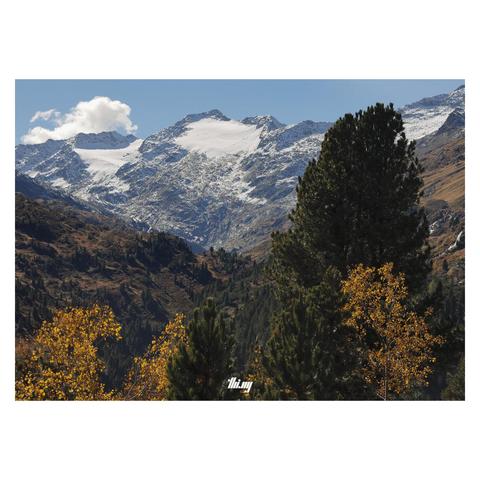 Beautiful, remote glacial high alpine landscape on a bright sunny day in autumn. The trees and meadows in the foreground are all in their best colors. Small water falls coming down on the right side. In the background, a majestic, still mostly glaciated mountain ridge of ~3500 meter peaks. Clear blue sky with a single small cloud.