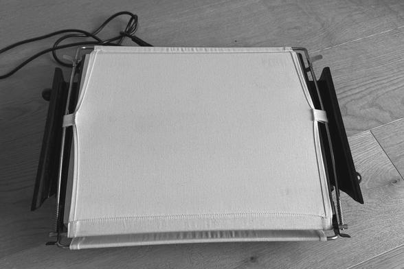 B&W photo of a dry press for baryta prints. The top part of the press is a sheet of thick canvas cloth, spanned over a slightly curved metal heat plate below.