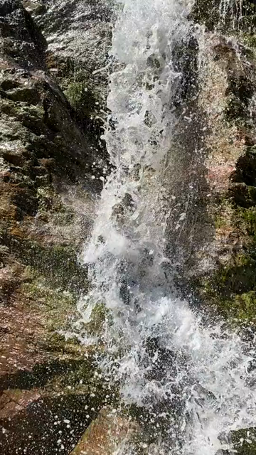 Short POV video of crossing a small waterfall in a high alpine landscape, the view panning 270 degrees to also capture the stunning opposite side of the valley and a short section of the semi-eroded path ahead...